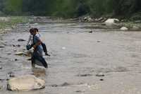 Una mujer cruza el río Minatitlán con un niño en brazos, luego que el ayuntamiento de Cuautitlán, Jalisco, ordenó derribar el puente colgante que comunica las comunidades de Paticajo y Plan de Méndez, Colima, con comunidades jaliscienses