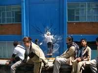 Un artista profesional pinta un mural en una secundaria, ante la mirada de algunos escolares.