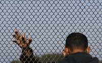 Migrante mexicano dialoga con un amigo en la malla que divide México de Estados Unidos, en la frontera de Tijuana