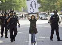 Escoltada por policías, una manifestante levanta un cartel de protesta por los altos precios del combustible, frente al edificio de ExxonMobil en Dallas, donde se realiza la asamblea anual de accionistas