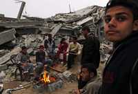 Palestinos damnificados se calientan en una fogata junto a las ruinas de sus casas destruidas por la ofensiva del ejército israelí